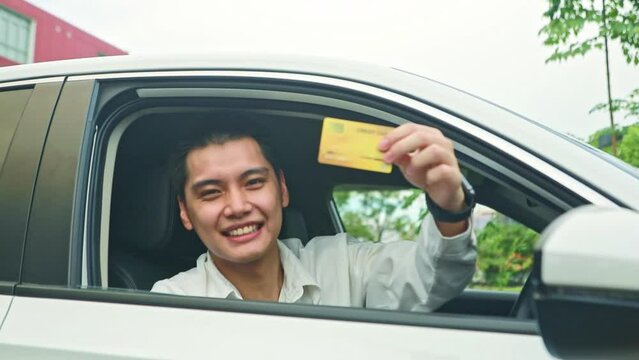 Portrait handsome asian gentleman driving car showing his member insurance card for customer peace of mind in using the car and driving safely with insurance policy.
