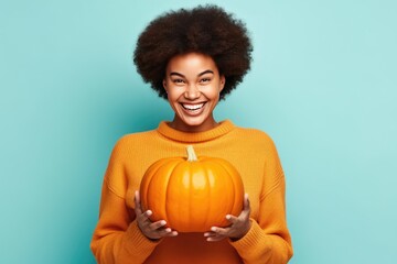 Attractive happy young black woman holding a pumpkin looking at the camera of cyan background - Powered by Adobe