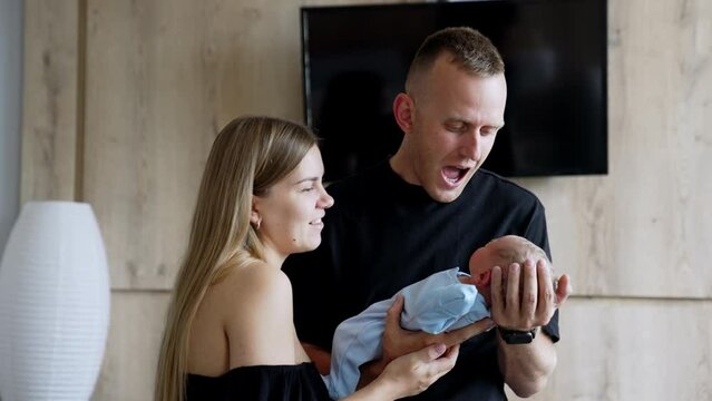 Happy couple looking at their newborn boy. Caucasian parents hold their baby talking to it.
