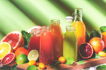 Citrus fruit juices, fresh and smoothies, food background. Summer drinks. Mix of different whole and cut fruits: orange, grapefruit, lime, tangerine with leaves and bottles with beverage