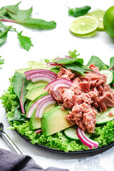 Canned tuna salad with avocado, cucumber, onion, spinach, lettuce and lime. White table background, top view