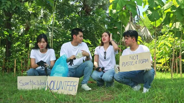 Group asian male and female volunteers sit wearing black gloves together cleaning preventing germs from dirt preparing pick up trash and preparing paper signs campaigning save the environment.