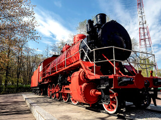 bright red steam locomotive in the city park in the form of a historical monument