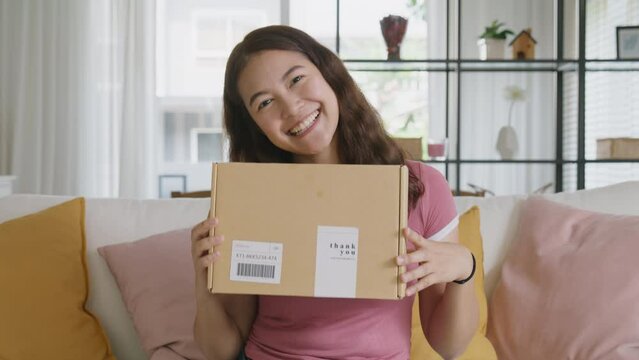 Young teen Gen Z girl asia people enjoy buy order gift postal parcel online shop. Happy receive courier carton box by fast express post mail omni channel retail store joy smile sitting at sofa home.