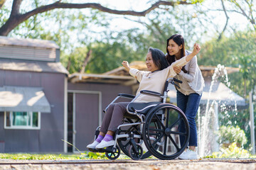 Asian senior woman in wheelchair with happy daughter. Family relationship retired woman sitting on wheelchair in the park age care at retirement home.