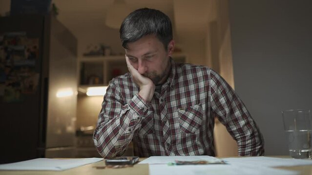 Financial problems. Sad man trying to find solution to taxes and debts at home in kitchen. Brainstorming ways of solving money troubles. Stressed male calculates costs, try to keep money in savings. 