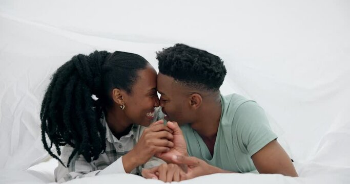 Black couple, bed and kiss with happy love under a bedroom blanket in the morning at home. Smile, funny and young people relax together with support and care in house with commitment and romance