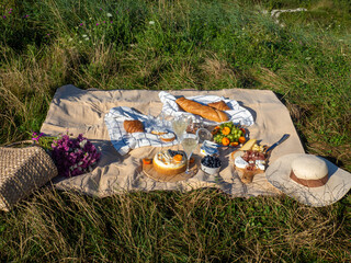 Beige blanket with fruits and pastries, cookies, berries, cheese, straw hat, baguette and bag with pink flowers. Concept of having picnic in a city park during summer holidays or weekends. Copy space.