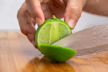 Female hand holding knife is cutting lime on a wooden board in Kitchen. Cutting fresh lemon in half close up. Hight Vitamin C Natural