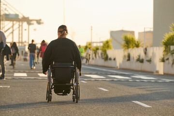 person in wheelchair at sunset on street in Malaga harbour in Spain