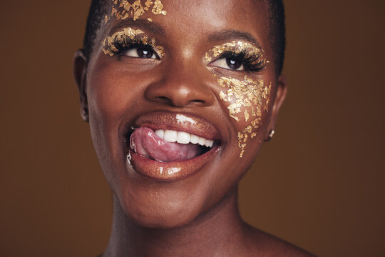 Gold, glitter and black woman beauty with makeup and tongue out in studio with sparkle cosmetics. Brown background, funny and female model with golden paint for skin glow and creative facial shine