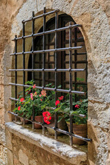 Fototapeta na wymiar Metal bars and flowers on an arched old window in Saint Paul de Vence, France