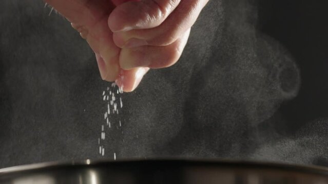 Slow motion man add salt into pot wit steam rising