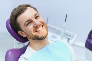 Handsome man smiling while teeth exam. Happy male patient sitting in a dentist's chair and having check up teeth.