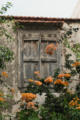Fototapeta na wymiar Old ancient colourful textured window in a stone wall and orange flowers in Greece, Crete. Traditional European, Greek architecture. Summer travel