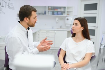 people, medicine, stomatology and health care concept - woman patient talking to male dentist and complain of toothache at dental clinic office.