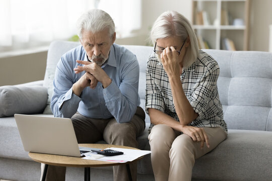 Worried senior retired husband and wife stressed about financial crisis thinking on problems, money troubles, overspending, sitting on home couch at laptop, calculator, paper bills, holding head