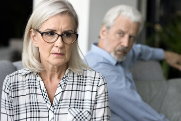 Stressed desperate mature wife feeling frightened with annoyed older husband behind, facing abuse, domestic violence. Senior couple getting relationship crisis, marriage problems