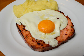 Pan-Fried Spicy Leberkase with Fried Egg Sunny Side Up and Mashed Potatoes on a White Plate