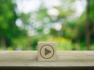 Play button icon on wood block cube on wooden table over blur green tree in park, Business music online concept