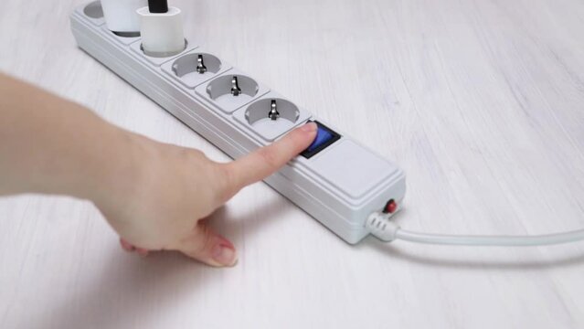 female hand turns on the power button on the surge protector power strip with sockets plugs, Electric plug put on multiple socket