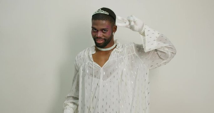 smiling beautiful transgender enjoying dancing in studio, blowing kiss, queen princess man has fun . Isolated white background Slow motion, bearded glamour man showing two fingers Love