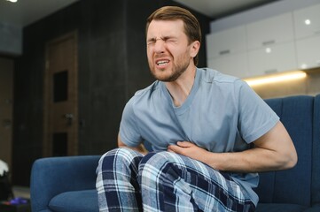 Fototapeta premium Young man suffering from stomach ache at home