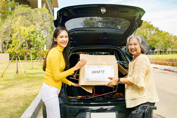 Photo shoot portrait elderly mother and her asian philanthropist daughter drive to the shelter donate wheelchairs and necessary charity clothes in cardboard boxes to the disabled and victims in need.