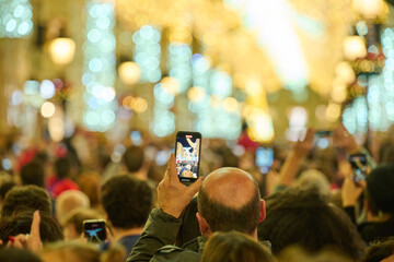 Man taking photo on phone in crowd at Calle Larios Christmas street in Malaga Spain