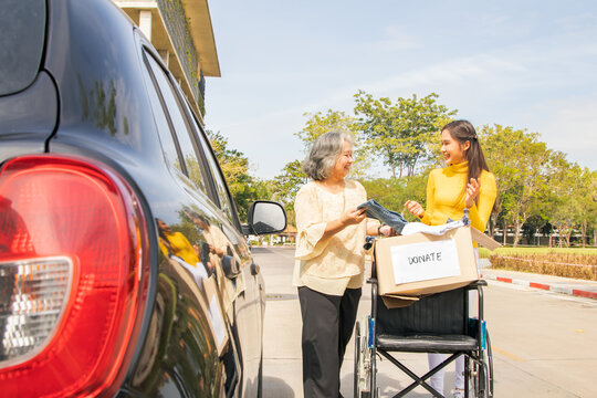 Happy elderly mother and her Asian philanthropist daughter drive to the shelter to donate wheelchairs and necessary charity clothes in cardboard boxes to the disabled and victims in need.