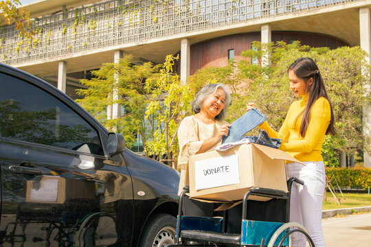 Elderly mother and her asian philanthropist daughter drive to the shelter to donate wheelchairs and necessary charity clothes in cardboard boxes to the disabled and victims in need.