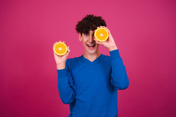 Funny attractive guy eats oranges. Pink background.