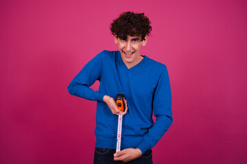 Funny attractive guy measures the length. Pink background.