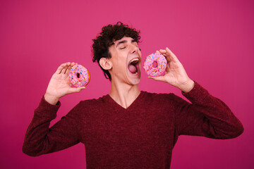 Funny attractive guy eats donuts. Pink background.