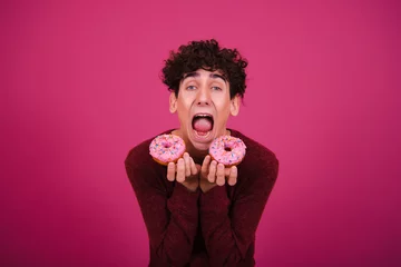 Fotobehang Funny attractive guy eats donuts. Pink background. © vladorlov