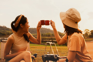 Wonderful evening moment : Two asian female friends sitting and chatting cheerfully drinking freshly brewed coffee watching the beauty of nature mountain forest and sunset on happy vacation trip. - Powered by Adobe