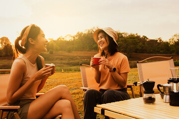 Wonderful evening moment : Two asian female friends sitting and chatting cheerfully drinking freshly brewed coffee watching the beauty of nature mountain forest and sunset on happy vacation trip.