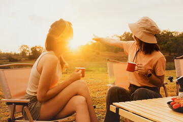 Wonderful evening moment : Two asian female friends sitting and chatting cheerfully drinking freshly brewed coffee watching the beauty of nature mountain forest and sunset on happy vacation trip. - obrazy, fototapety, plakaty