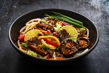 Asian food - roast beef, noodles and stir fried vegetables on wooden table
