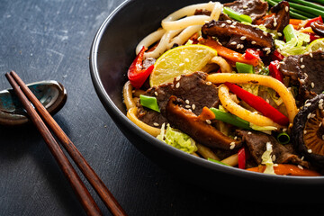 Asian food - roast beef, noodles and stir fried vegetables on wooden table
