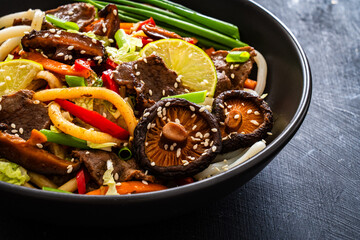 Asian food - roast beef, noodles and stir fried vegetables on wooden table
