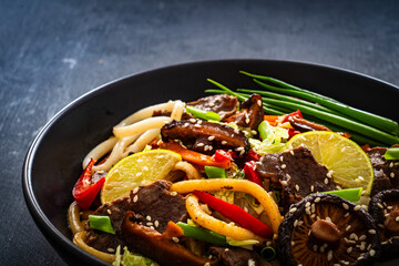Asian food - roast beef, noodles and stir fried vegetables on wooden table
