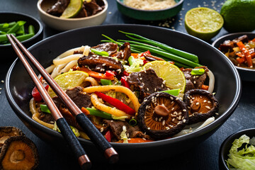 Asian food - roast beef, noodles and stir fried vegetables on wooden table
