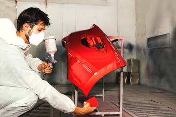 Male auto painter working car painting room inspects and compares the red paint to the sheet metal sprayed front bumper to get similar and beautiful color : Jobs in auto repair garages.