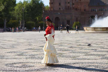 Young black woman dressed as a flamenco gypsy in a square in Seville, Spain. She wears a beige...
