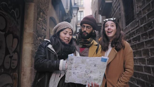 Cheerful young tourist friends looking at city map during winter vacations, sightseeing old historical town