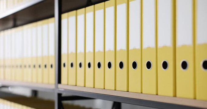 Yellow folders put in long line on shelf of rack in light office. Organized structure of document ring binders with accounting materials for work slow motion