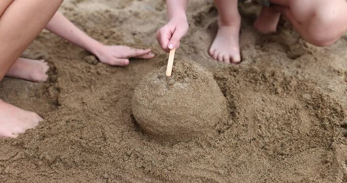 Barefoot children build sand structure banging wooden stick on beach. Concept of entertainment and activities in childhood slow motion