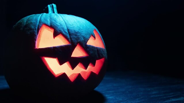 Halloween pumpkin with scary face at dark background. Pumpkin glows on Halloween night. Halloween concept. Close-up in 4K, UHD