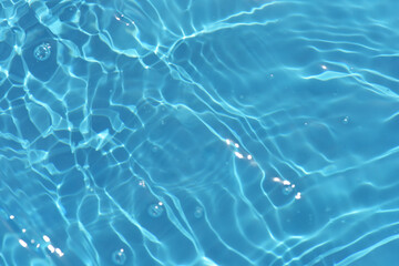 Blue water with ripples on the surface. Defocus blurred transparent blue colored clear calm water surface texture with splashes and bubbles. Water waves with shining pattern texture background.